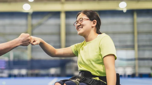 A young wheelchair user smiling and fist-bumping in a sports hall
